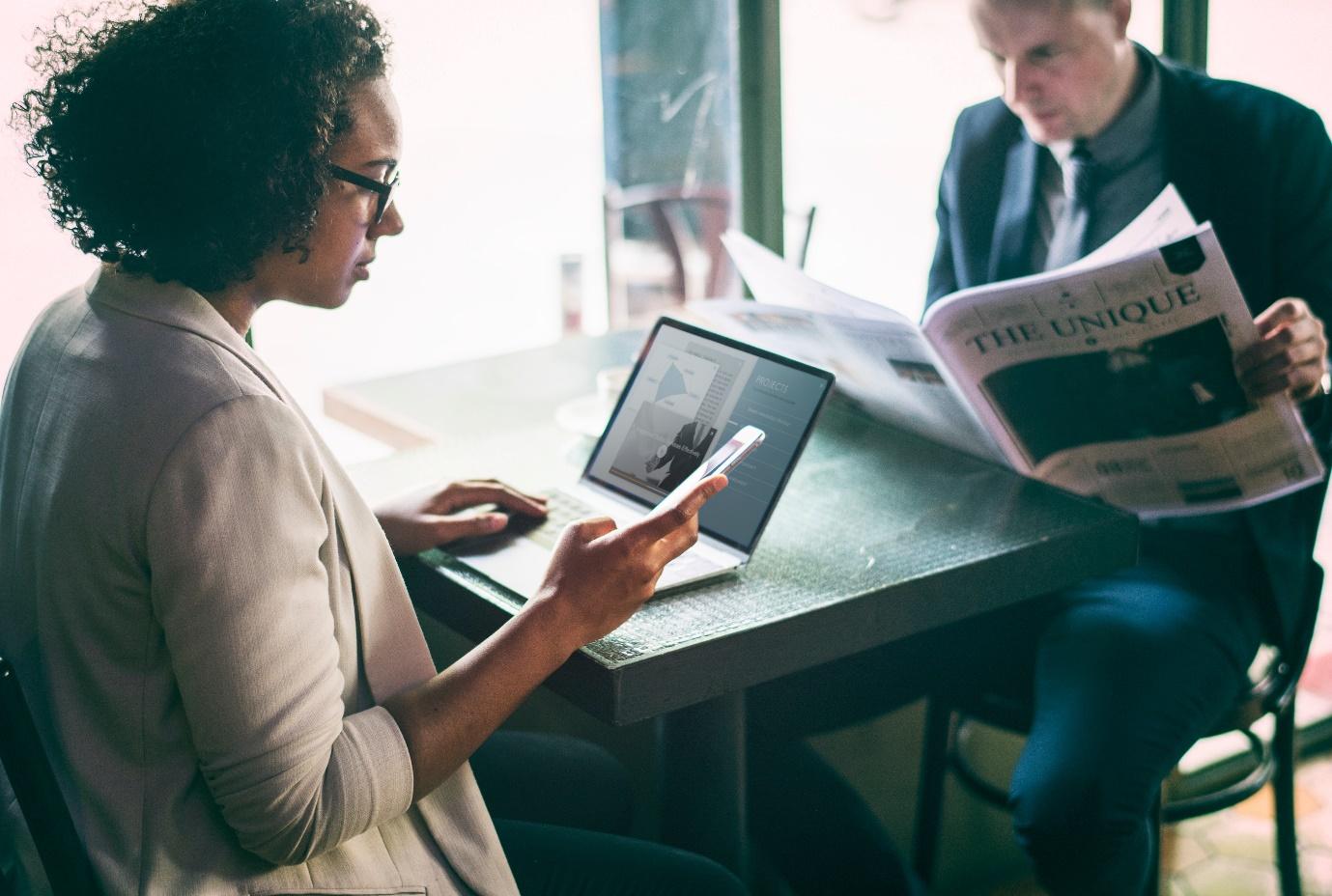 Lady Doing Work on Her Laptop Whilst Her Friend Is Reading a Newspaper